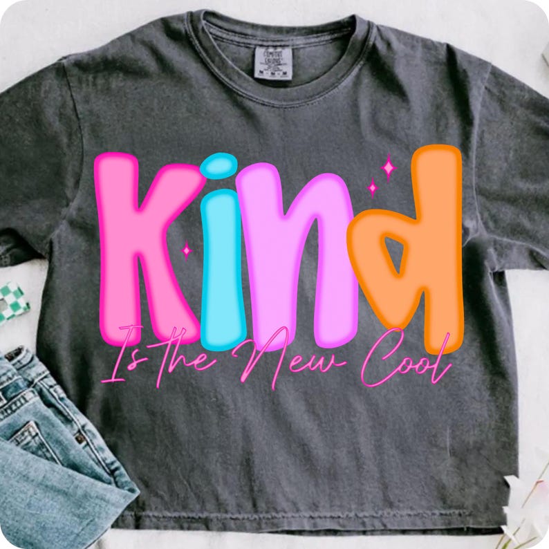 A close-up of the 'Kind Is The New Cool' Preppy PNG design on a white t-shirt, showcasing retro varsity letters and checkerboard elements.